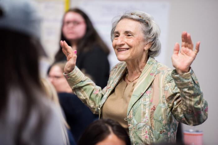 Older female educator standing in classroom with raised hands and smiling