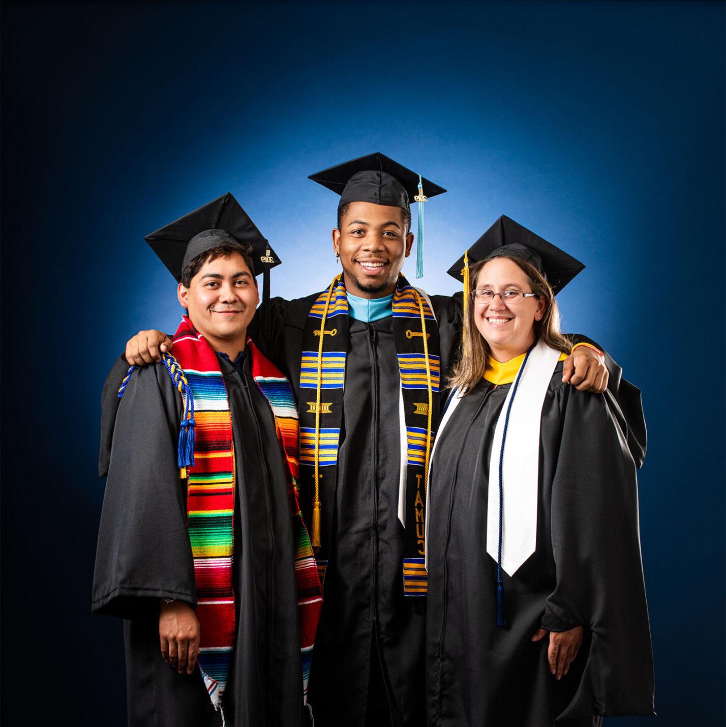 三个学生戴着帽子，穿着长袍，对着镜头微笑. 