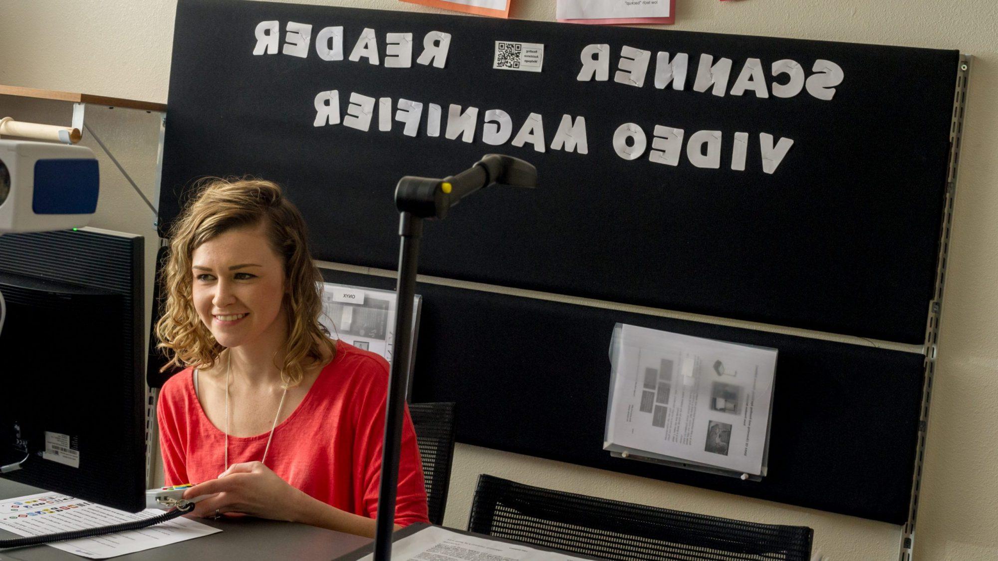 一名女学生站在一个写着扫描仪阅读器视频放大镜的牌子前.