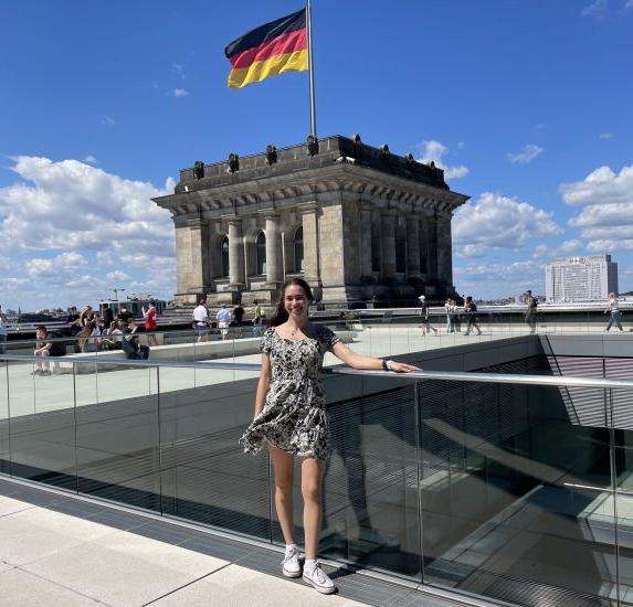 一位年轻女性站在悬挂德国国旗的建筑物前.